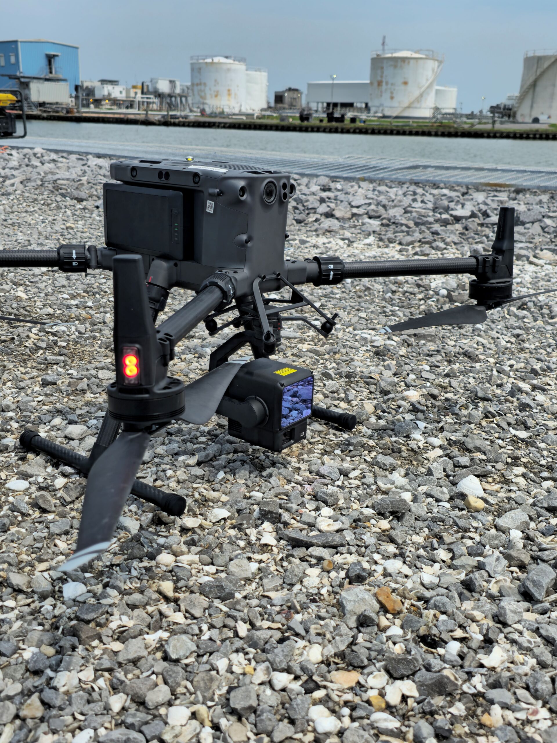 Drone equipped with a LiDAR sensor on a gravel shoreline near an industrial site